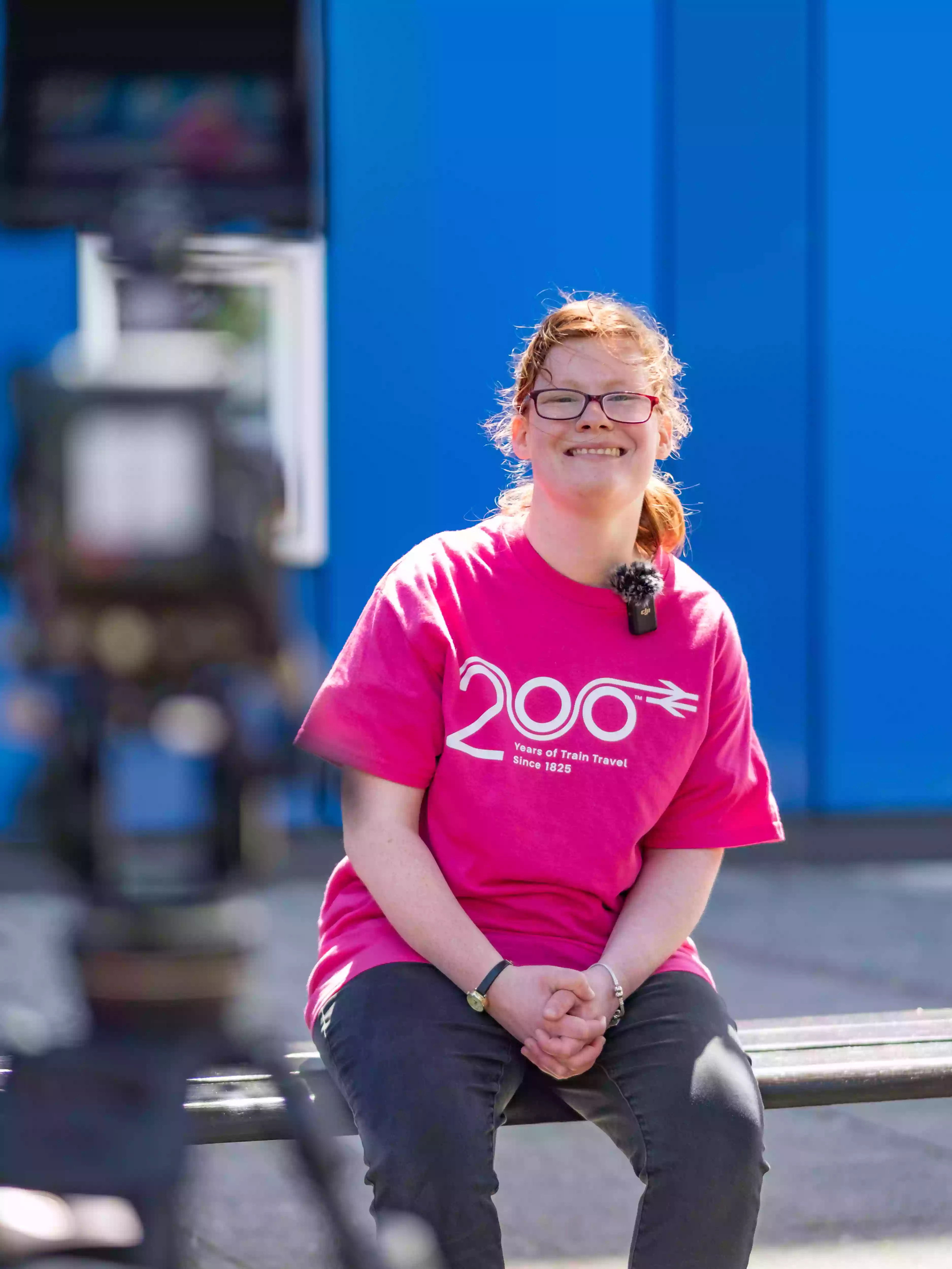 A COPC student wearing a pink Railway 200 t-shirt smiling during a behind-the-scenes interview after the community flashmob performance in Portsmouth