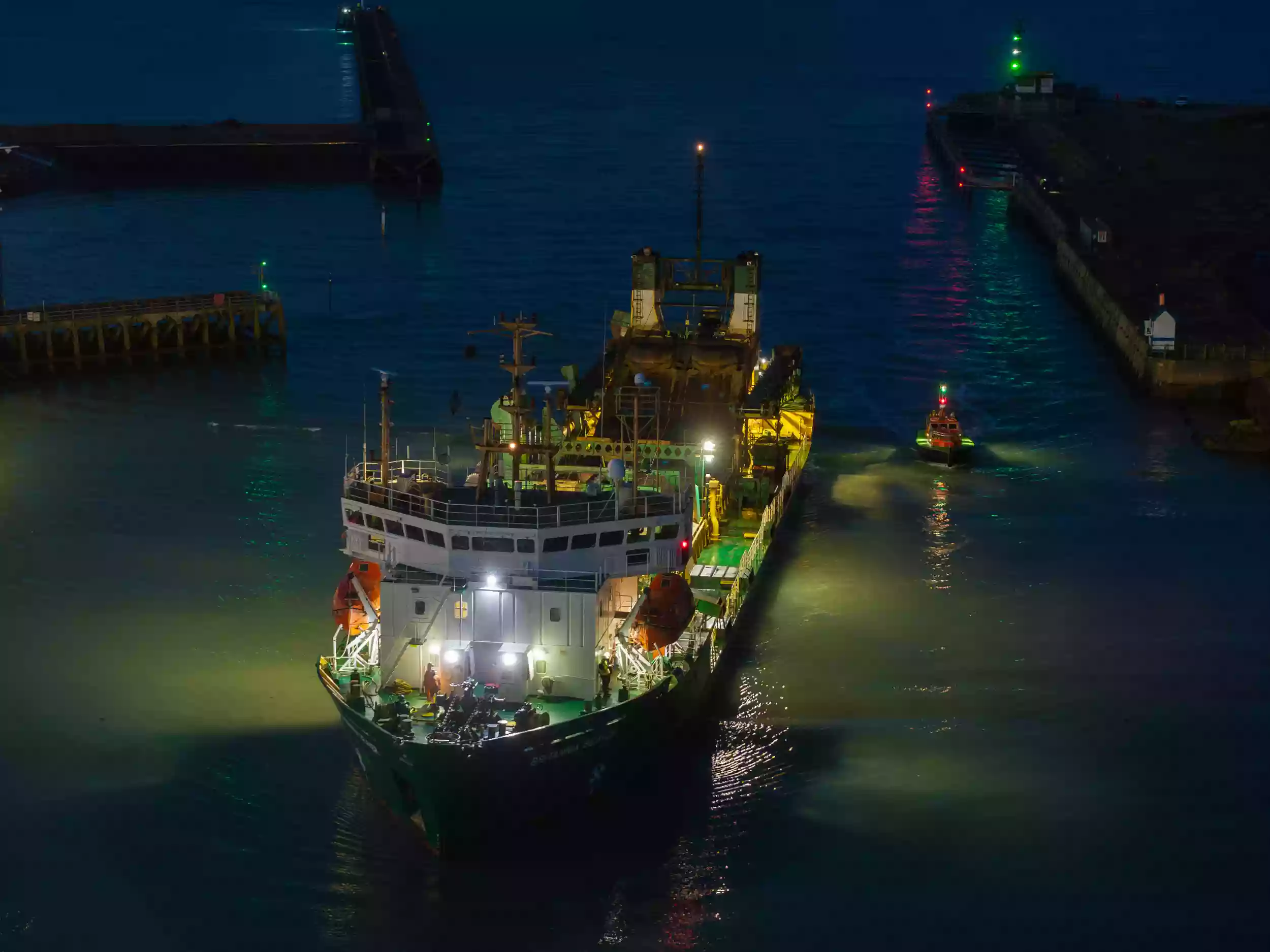 Top-down aerial drone photograph of the Britannia Beaver dredger at night, with the vessel's deck and hopper lit by onboard lighting.