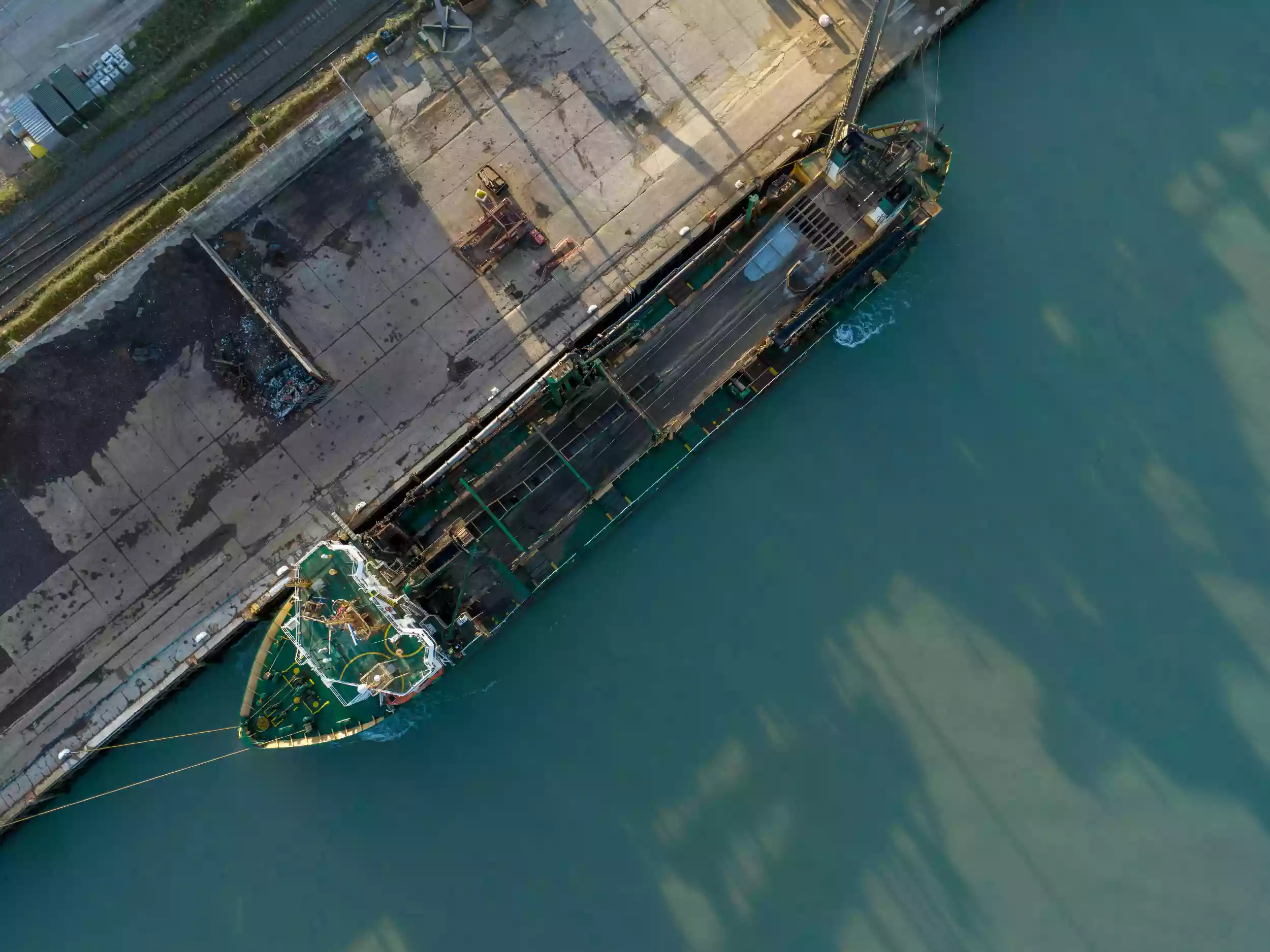 Aerial drone view of the Britannia Beaver moored in an active working port, with cranes and dockside operations visible nearby.