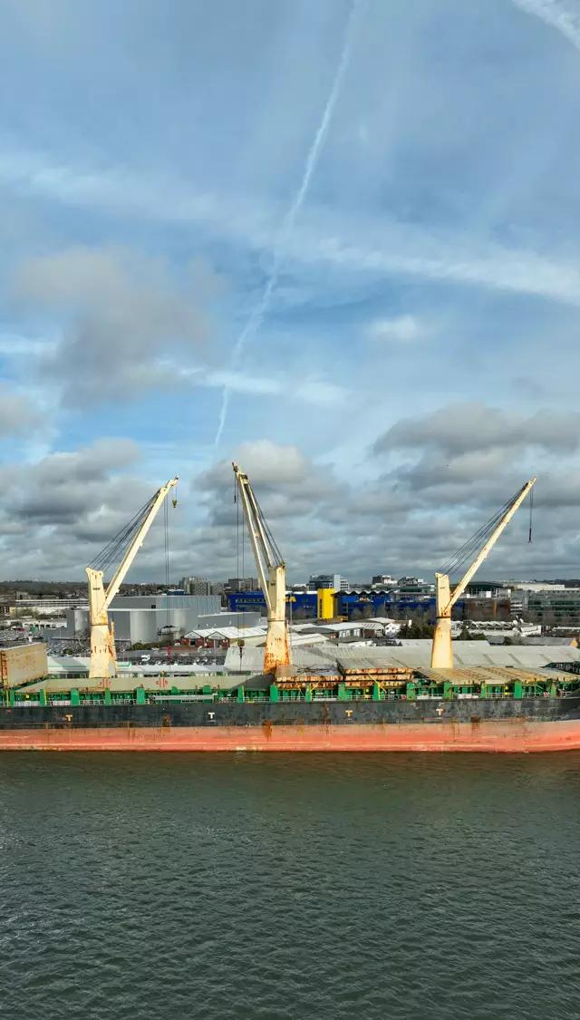 Heavy-lift cargo ship with deck cranes raised, moored at the Port of Southampton under a cloudy sky