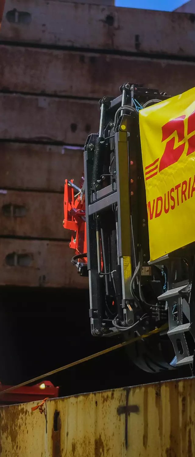 DHL Industrial Projects banner on a Terex tracked machine being lowered into the ship's hold