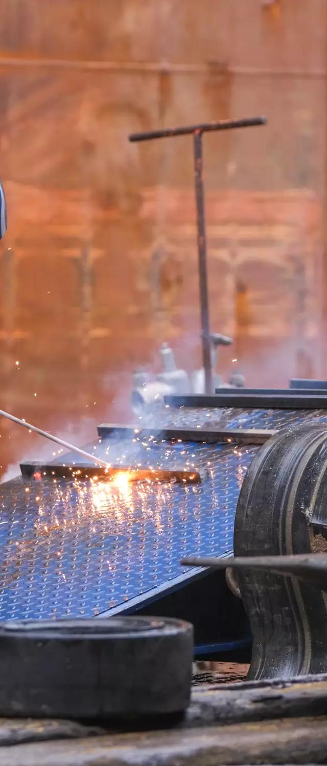 Worker welding sea fastenings in the ship's hold to secure heavy machinery for the voyage to Brisbane