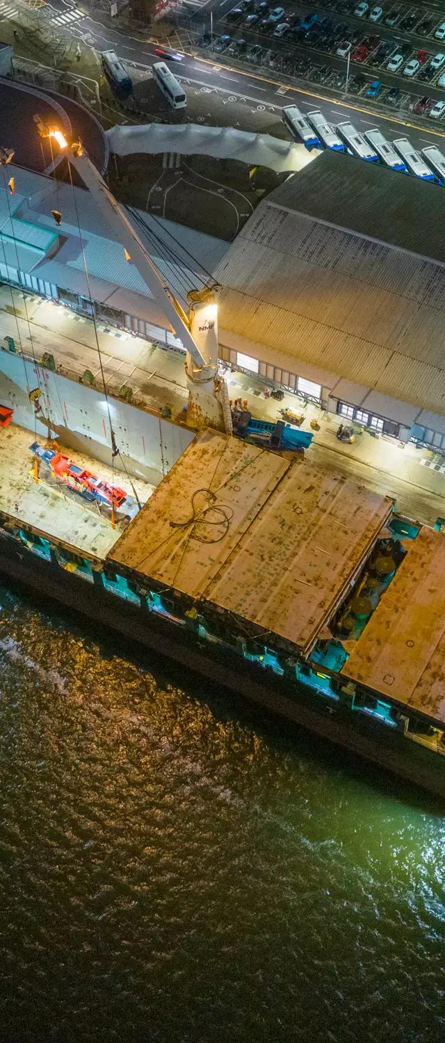 Drone view at night of the cargo ship's lit deck and open holds during loading at ABP Southampton