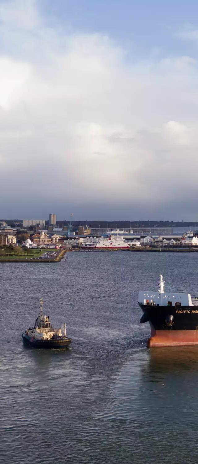 Aerial view of the loaded cargo ship and tug leaving the Port of Southampton, bound for Brisbane